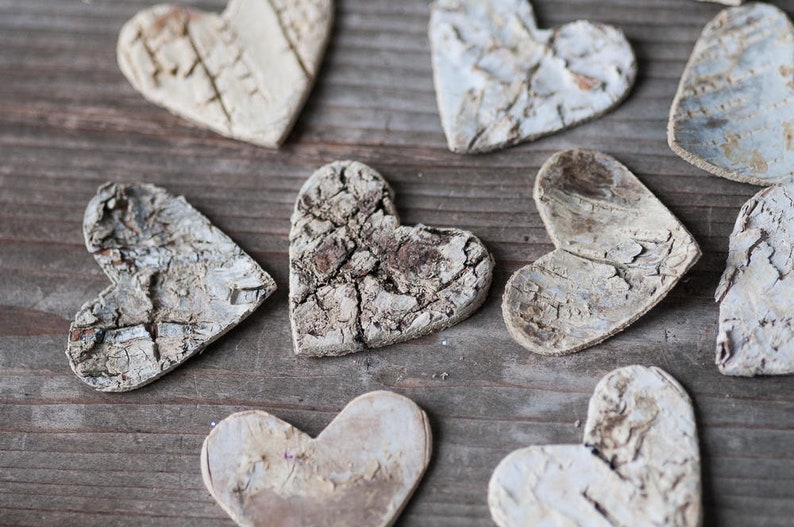 May include: A collection of rustic, white, wooden heart-shaped ornaments with a natural, bark-like texture. The hearts are arranged on a wooden surface.