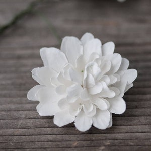 May include: A single white paper flower with multiple layers of petals. The flower is on a wood background.