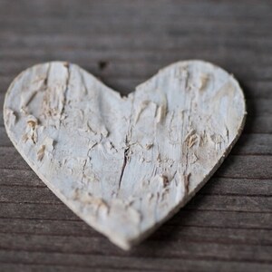May include: A white wooden heart with a distressed finish, resting on a wooden surface.