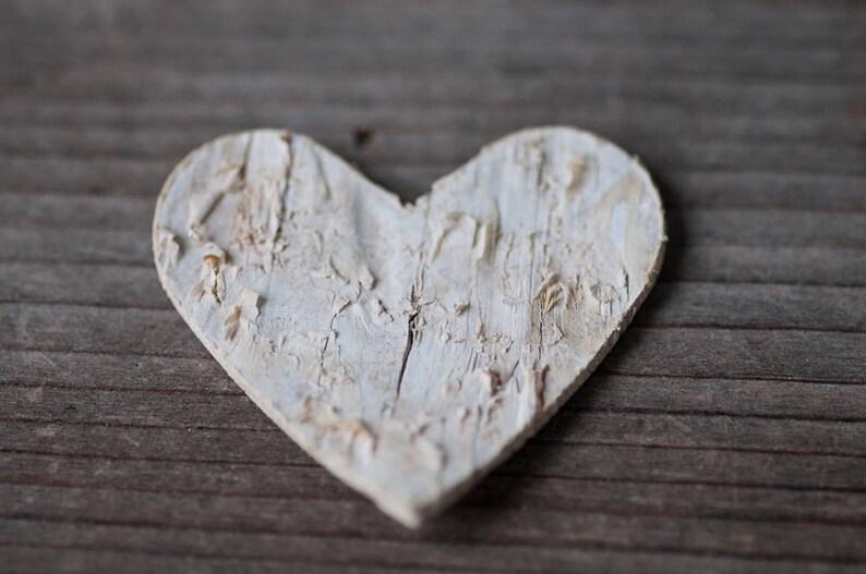 May include: A white wooden heart with a distressed finish, resting on a wooden surface.