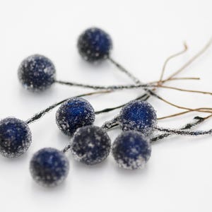 May include: A cluster of seven blue berry-shaped ornaments with a frosted finish, each attached to a thin brown twig.