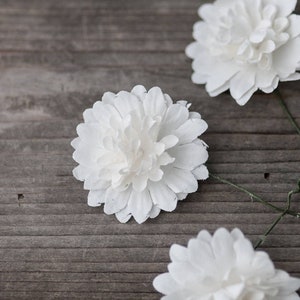 May include: Three white paper flowers with green stems on a wooden surface.