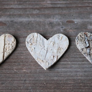 May include: Three white wooden hearts with a wood grain texture, arranged in a row on a wooden surface.
