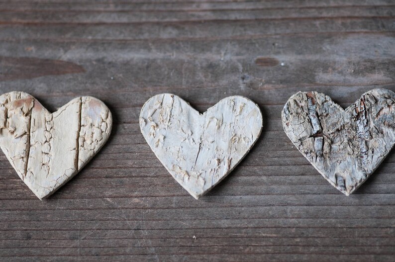 May include: Three white wooden hearts with a wood grain texture, arranged in a row on a wooden surface.