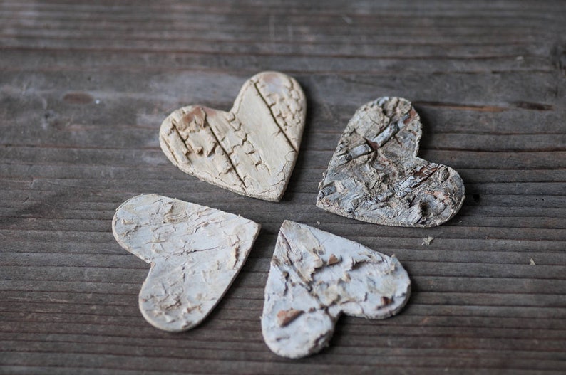 May include: Four white wooden hearts with a rustic, distressed finish. The hearts are arranged in a flower shape on a wooden surface.