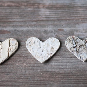 May include: Three white wooden hearts with a rustic, textured finish, arranged in a row on a weathered wooden surface.