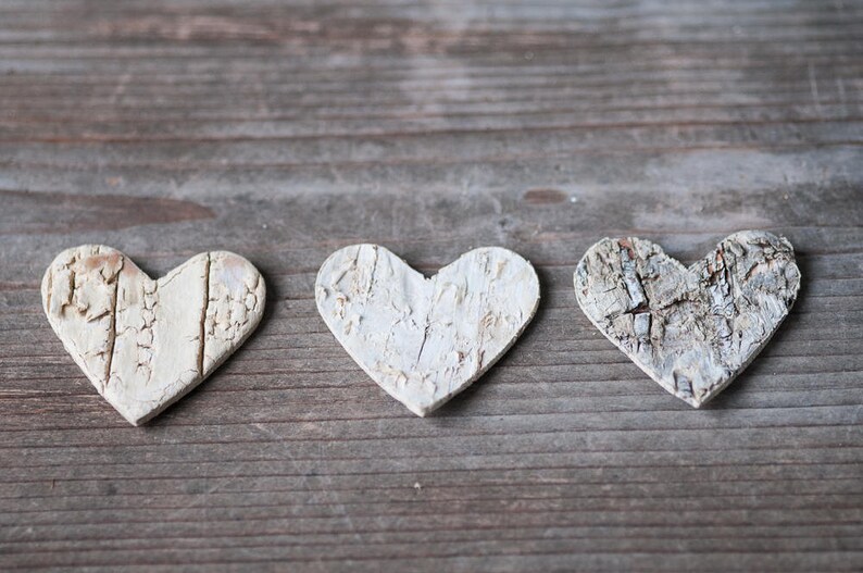 May include: Three white wooden hearts with a rustic, textured finish, arranged in a row on a weathered wooden surface.