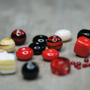 May include: A collection of colourful glass beads in red, black and white. The beads are round and have a smooth, glossy finish.