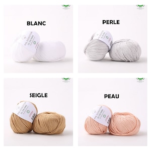 May include: Eight balls of yarn in different colors, including white, gray, beige, brown, and pink. Each ball has a label with the name of the color in French.