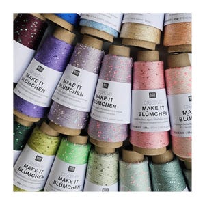 May include: A selection of colourful thread spools, with shades of purple, pink, green, and blue. Each spool is labelled with the text "creative MAKE IT BLÜMCHEN". The thread is decorated with sequins.