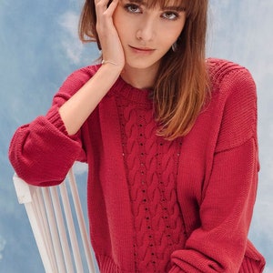May include: A red cable knit sweater with a loose fit and long sleeves. The sweater has a delicate openwork pattern.