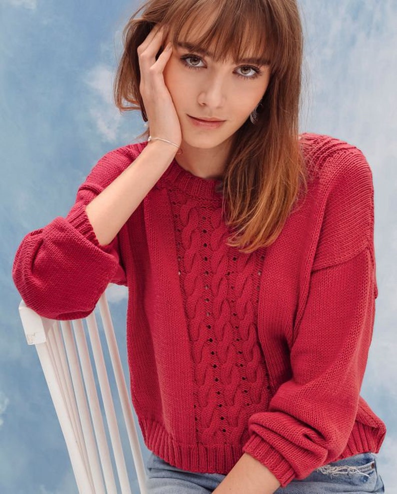 May include: A red cable knit sweater with a loose fit and long sleeves. The sweater has a delicate openwork pattern.