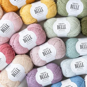 May include: A selection of pastel-coloured skeins of Drops Belle yarn, including pink, yellow, green, and blue. Each ball has a label that reads "DROPS BELLE UNI COLOUR Everyday luxury!" The yarn is arranged closely together, ideal for knitting or crochet projects.