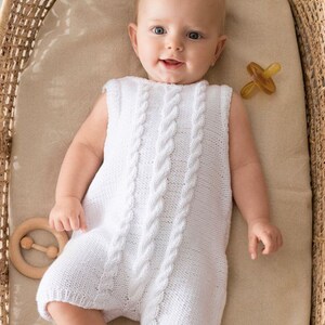 May include: A white knitted baby romper with a cable knit pattern. The romper is sleeveless and has a round neckline. The baby is lying on its back in a wicker basket.