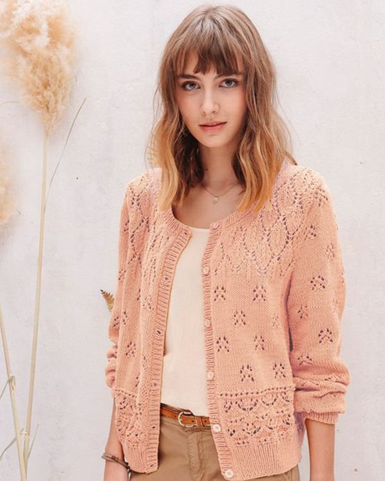 May include: A light pink knitted cardigan with a delicate lace pattern. The cardigan has a button-up front and long sleeves.
