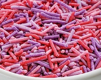 Puede incluir: Un tazón blanco lleno de espolvorear rosa y morado. Los espolvorear son largos y delgados, y son perfectos para decorar pasteles y magdalenas.