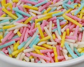 Puede incluir: Un bol blanco lleno de espolvorear de colores. Las chispas son largas y delgadas, y son en tonos de rosa, azul, amarillo y blanco.