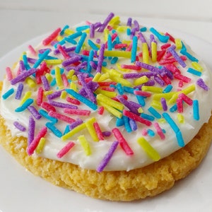 Puede incluir: Una galleta redonda de az&uacute;car cubierta con glaseado blanco y espolvoreada con coloridos sprinkles.