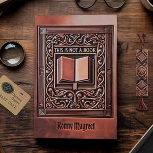 Op de afbeelding: Een bruin lederen gebonden dagboek met een sierlijk koperkleurig ontwerp. Het dagboek bevat de tekst "Dit is geen boek" en de naam "Ronny Magreet".