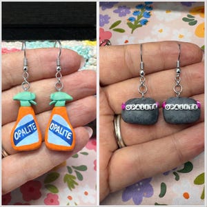 May include: Handmade earrings featuring miniature orange and blue spray bottles with the word "OPALITE" on the label. The other pair of earrings have gray stone-like beads with the word "OPALITE" spelled out in white beads.