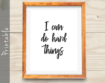 May include: A printable wall art print with a wooden frame. The print features the text "I can do hard things" in black cursive font on a white background.