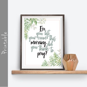 May include: A framed print with the text "Ere you left your room this morning, did you think to pray?" in black and gray script. The print is decorated with watercolor greenery and is displayed on a wooden shelf with a gold geometric vase.