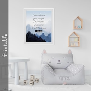 Op de afbeelding: Een wit ingelijst print met een blauwe aquarel achtergrond en een citaat uit de Bijbel: "Ik heb je gebed gehoord, ik heb je tranen gezien: Ik zal je genezen. 2 Koningen 20:5". De print hangt aan een witte muur boven een grijze, kattenvormige zitzak met de tekst "Cutty Cat" gedrukt op de voorkant.