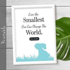 May include: A white framed print with a blue silhouette of a rabbit in a field of grass. The print features the quote "Even the smallest one can change the world." with the attribution "Peter Rabbit".
