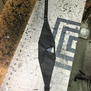 Peut inclure: Un masque en cuir noir avec un petit trou pour l'&oelig;il et une sangle qui se boucle &agrave; l'arri&egrave;re.