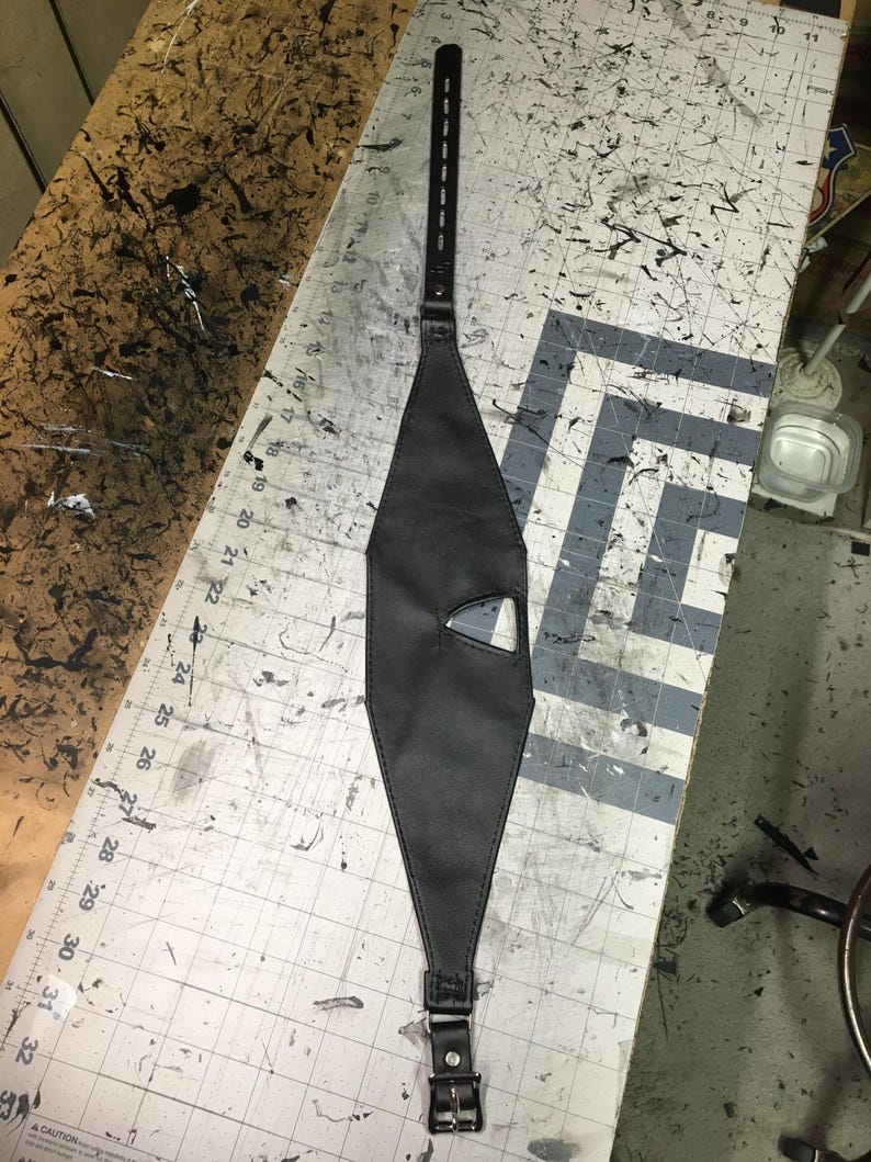 Peut inclure: Un masque en cuir noir avec un petit trou pour l'&oelig;il et une sangle qui se boucle &agrave; l'arri&egrave;re.