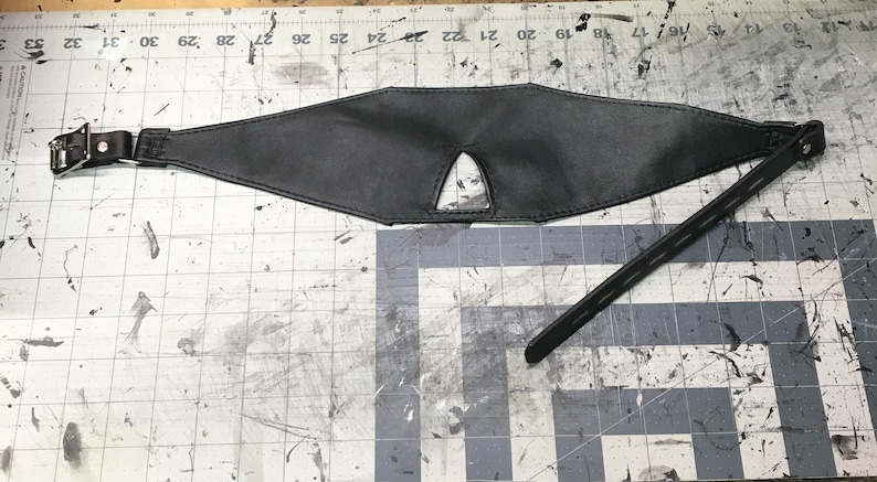 Peut inclure: Un bandeau en cuir noir avec un petit trou pour les yeux au centre. Le bandeau est attach&eacute; &agrave; une longue sangle avec une boucle en m&eacute;tal.