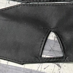 Peut inclure: Un bandeau en cuir noir avec une d&eacute;coupe triangulaire pour la vision. Le bandeau est dot&eacute; de sangles r&eacute;glables avec des boucles m&eacute;talliques.