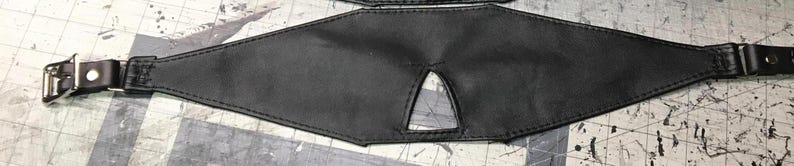 Peut inclure: Un bandeau en cuir noir avec une d&eacute;coupe triangulaire pour la vision. Le bandeau est dot&eacute; de sangles r&eacute;glables avec des boucles m&eacute;talliques.