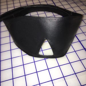 Peut inclure: Un bandeau en cuir noir avec une d&eacute;coupe triangulaire pour le nez.