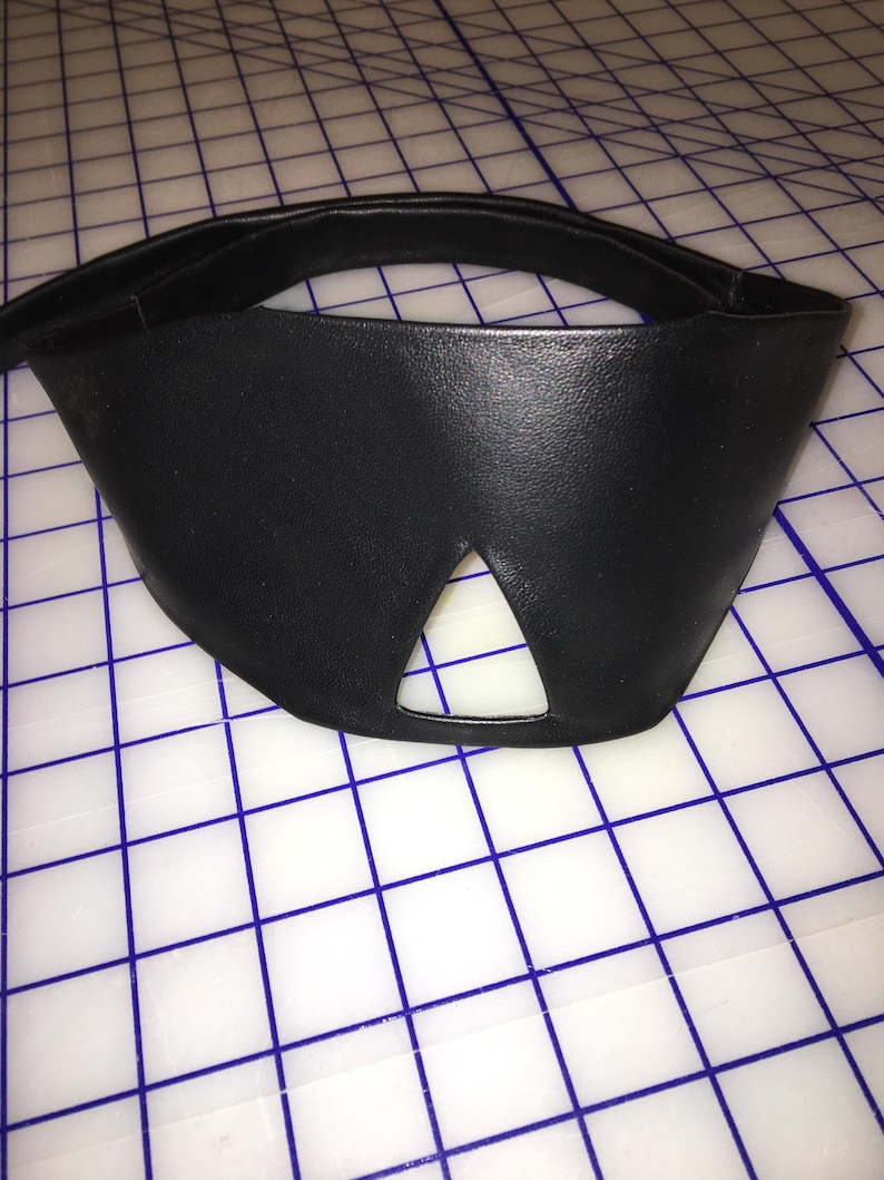 Peut inclure: Un bandeau en cuir noir avec une d&eacute;coupe triangulaire pour le nez.