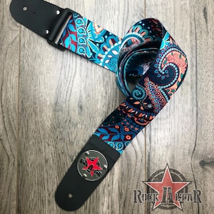 May include: A guitar strap featuring a vibrant paisley pattern in shades of teal, dark blue, and coral orange. The strap includes black leather ends with silver rivets and a circular metal emblem displaying a red star and the text Rock Altar.