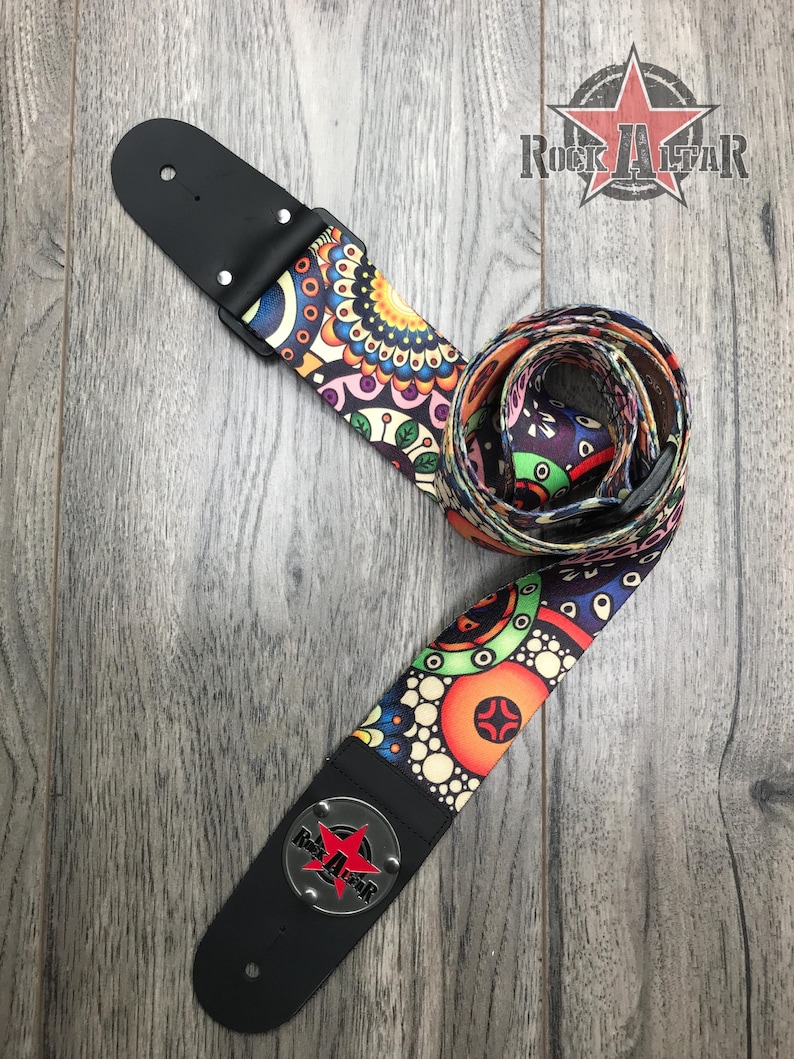 May include: A guitar strap featuring a vibrant, multicolored geometric and floral pattern on a dark background. The strap includes black leather ends with metal rivets and a circular silver-toned emblem displaying the Rock Altar logo with a red star.
