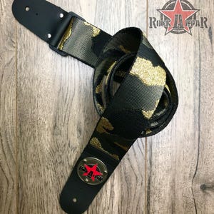May include: A guitar strap featuring a black and metallic gold camouflage pattern. The strap includes black leather ends with silver rivets and a circular metal emblem displaying a red star and the text Rock Altar in black lettering.