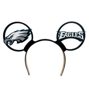 May include: Black and white Mickey Mouse ears headband with a Philadelphia Eagles logo on one ear and a stylized eagle on the other ear.