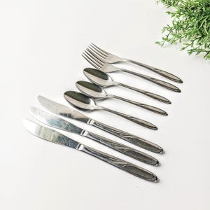 May include: A set of stainless steel cutlery with a decorative floral design. The set includes a fork, two knives, and four spoons.