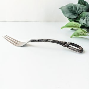 May include: A silver fork with a twisted, dark brown handle. The handle is shaped like a knot.