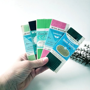 May include: Five rolls of 1/2 inch wide seam binding in various colors, including pink, green, and blue. The labels say "Seam Binding", "Non-Shrink", "Wrights Trims", and "Guaranteed Color Fast".
