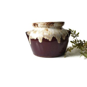 May include: A brown and white glazed ceramic pot with a rounded shape and two handles. The pot has a drip glaze effect, with white glaze dripping down from the top of the pot.