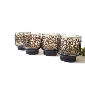 May include: Set of four brown glass tumblers with a decorative etched design. The glasses have a wide base and a flared top.