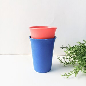 May include: Two plastic cups stacked on top of each other. The top cup is a bright coral color and the bottom cup is a dark blue.