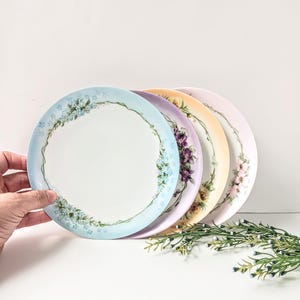 May include: Four floral patterned dessert plates in shades of blue, purple, yellow, and pink. The plates are stacked on top of each other, with the blue plate on top.