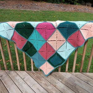 May include: A crocheted blanket with a patchwork design featuring squares in shades of pink, peach, teal, and green.