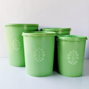 May include: Four green plastic containers with lids. Each container has a white floral design. The containers are different sizes, with the largest one on the left. The lids are the same green color as the containers.