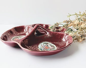 May include: A three-sectioned serving dish with a handle. The dish is made of red ceramic with gold accents and features a floral pattern. Each section has a painted scene of people in a garden.
