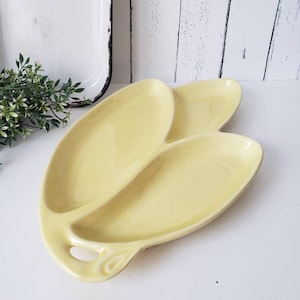 May include: A yellow ceramic serving dish with three sections. The dish is shaped like a flower with a handle.